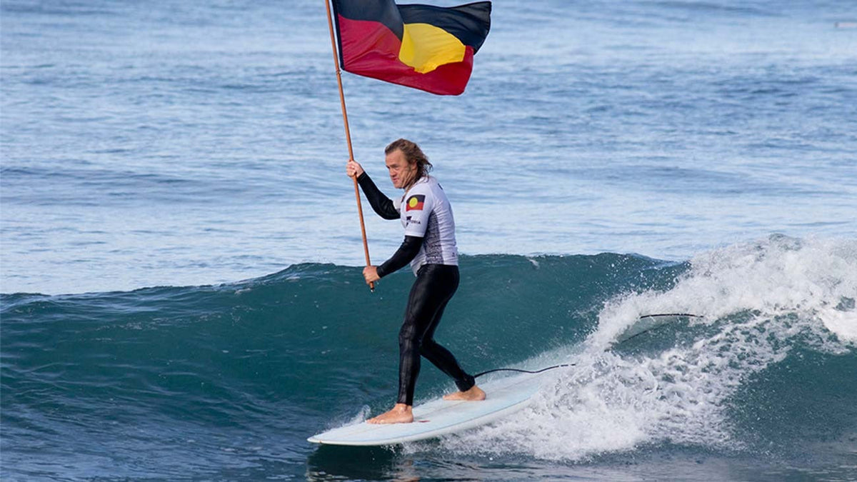 Person surfing Bells Beach with the aborignal flag