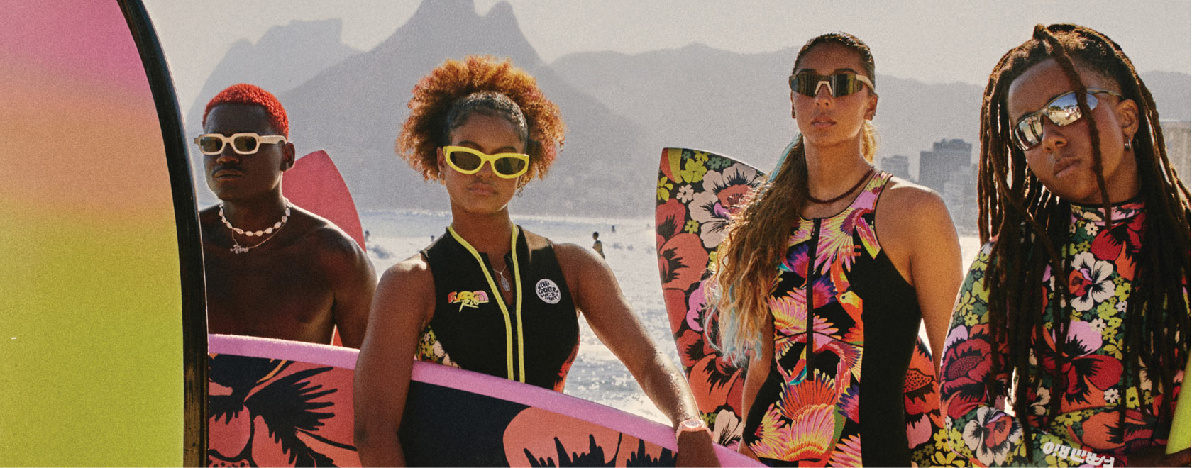 Four people with colorful surfboards and sunglasses against a mountainous background