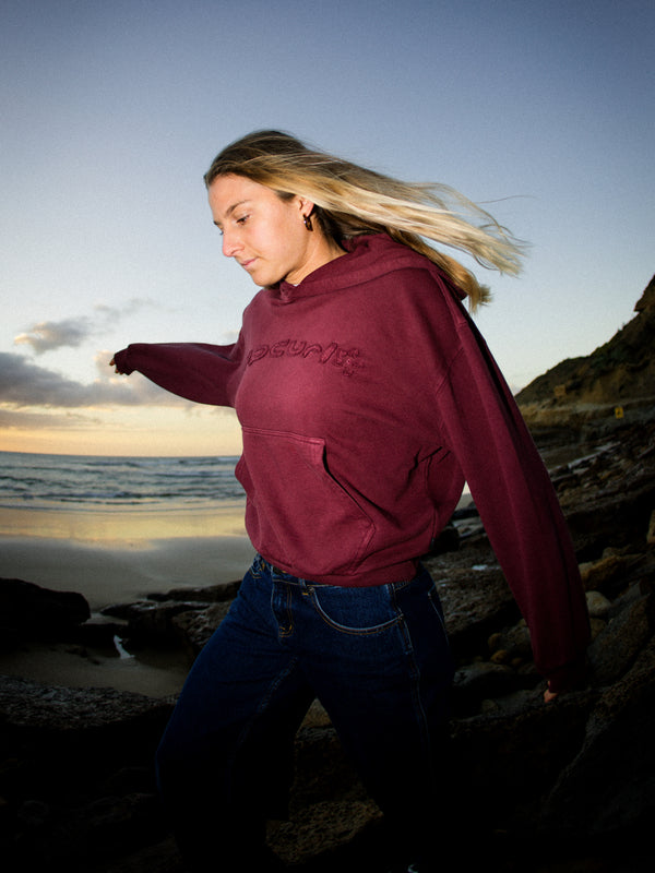 Person wearing a maroon hoodie on a beach at sunset
