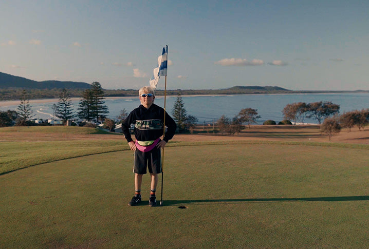 Person standing on a golf course with a scenic background of water and trees.