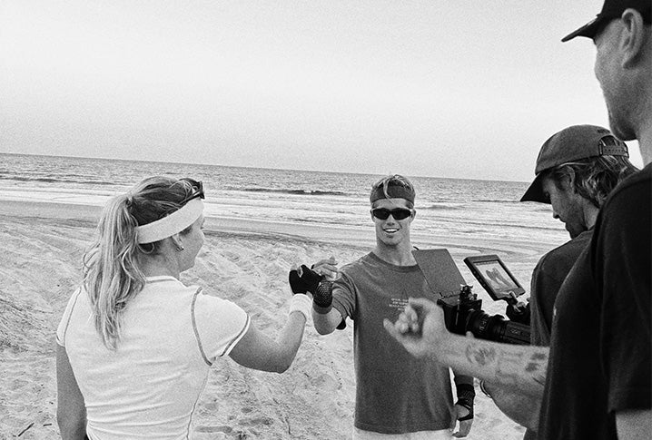 Group of people on a beach with one person holding a camera and another holding a tablet.