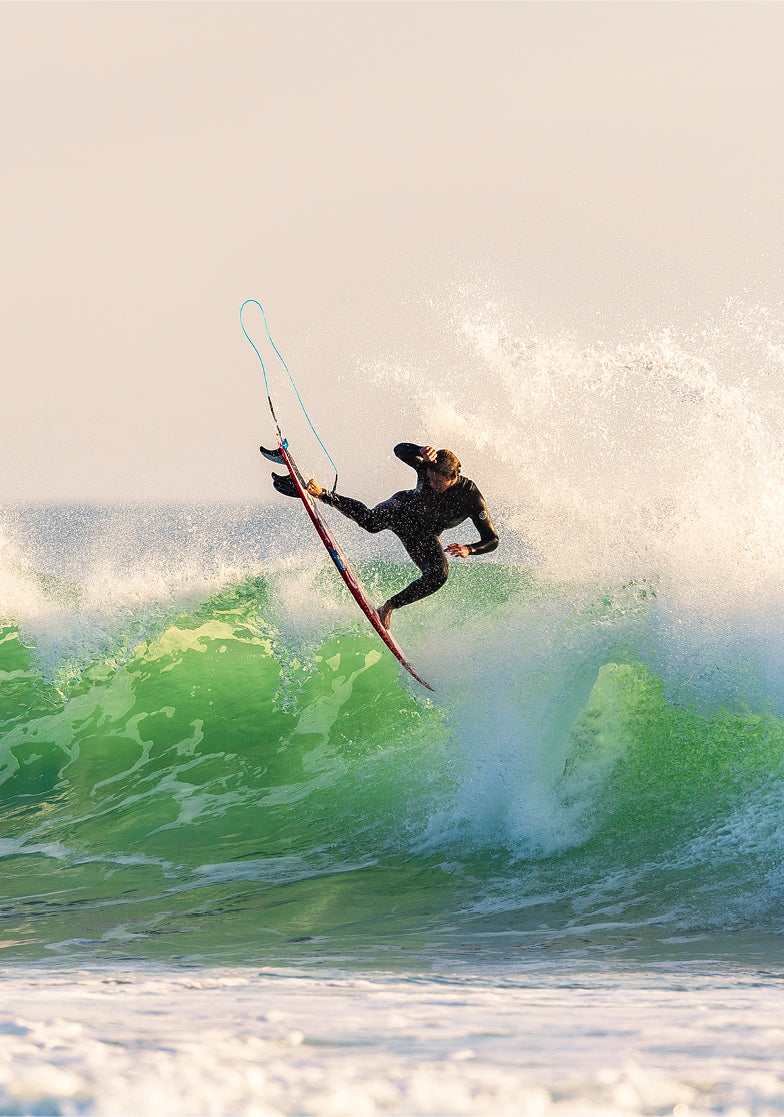 Person surfing on a large wave with a sunset or sunrise in the background