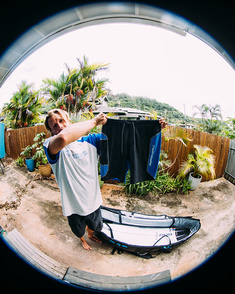 Person holding a kayak and dry bag outdoors with plants and a fence in the background