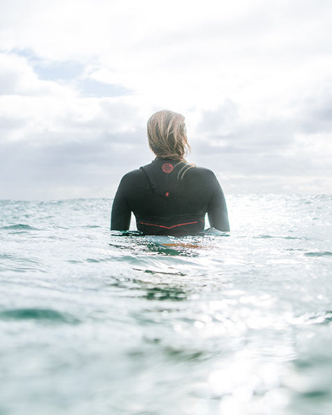 Person in a wetsuit standing in the ocean with a cloudy sky.