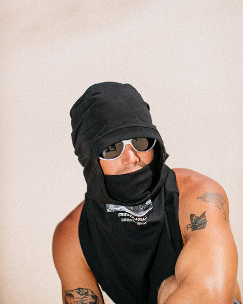Person wearing a black t-shirt and sunglasses with tattoos on arms against a beige background