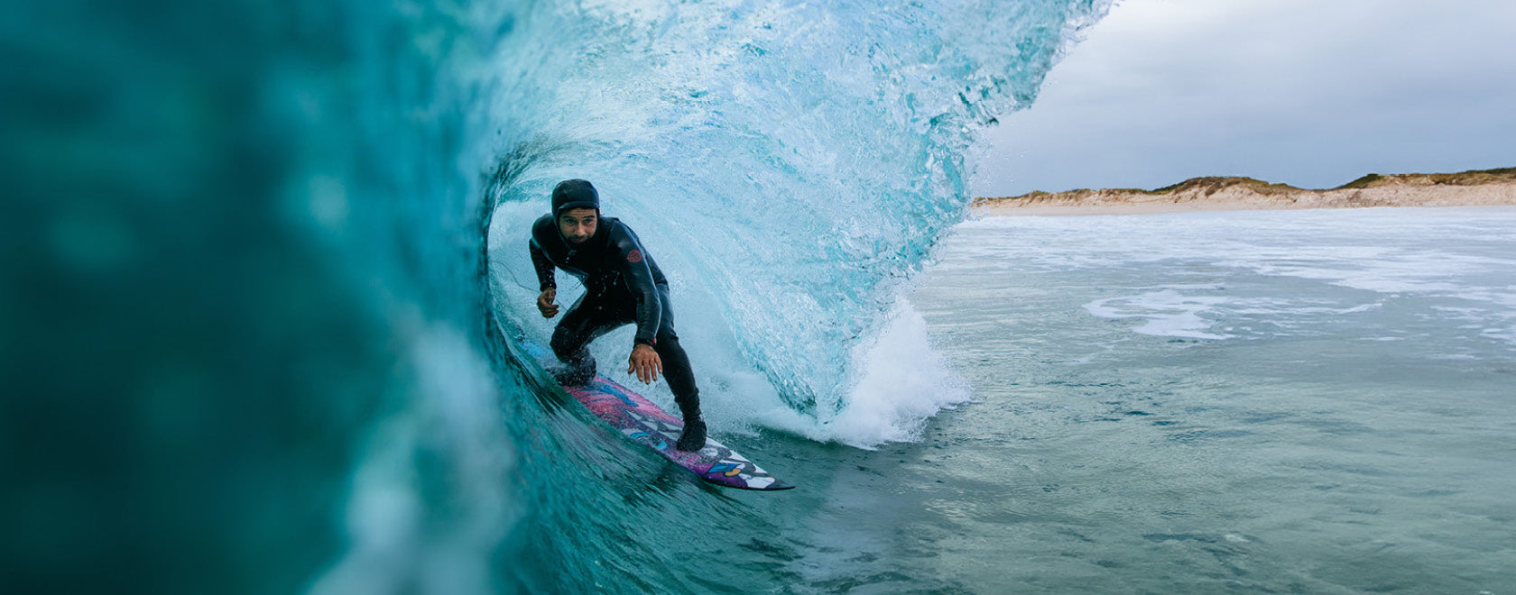 Person surfing inside a blue wave with a beach in the background