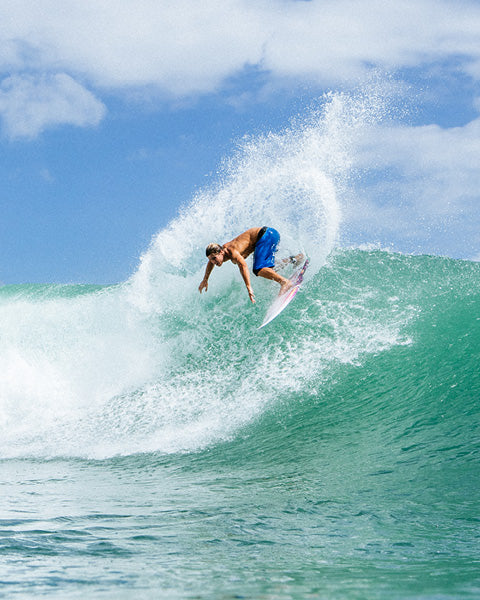 Surfer in blue shorts riding a wave with a clear sky background