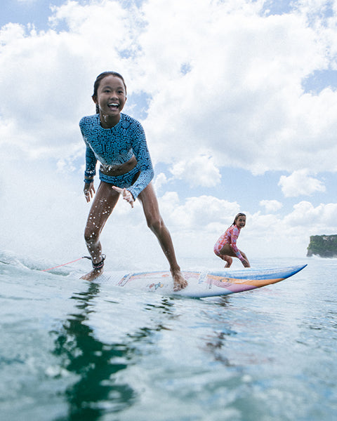 Two people surfing on a clear day with blue skies and green water.