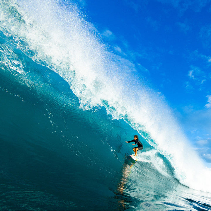 Surfer riding a large wave with blue sky and ocean.