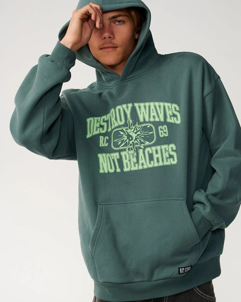 A person wearing a muted teal-green pullover hoodie with a light green graphic print on the front that reads 'DESTROY WAVES RC 69 NOT BEACHES' with a sunburst design. The photo is cropped from the chest up against a plain light gray studio background.