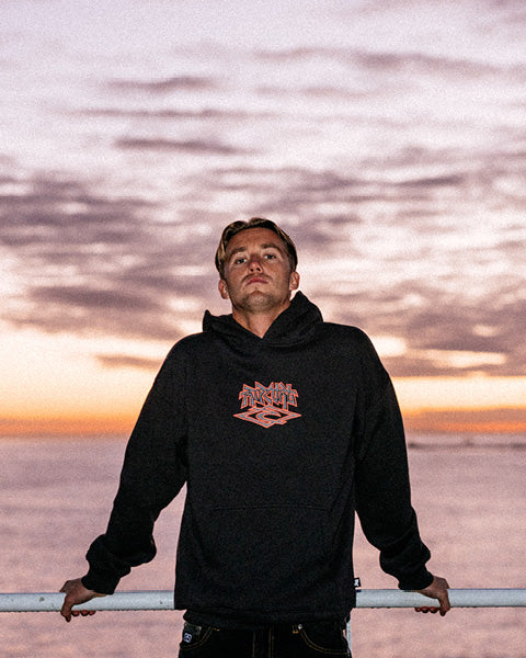 Person wearing a black hoodie with a logo against a sunset sky