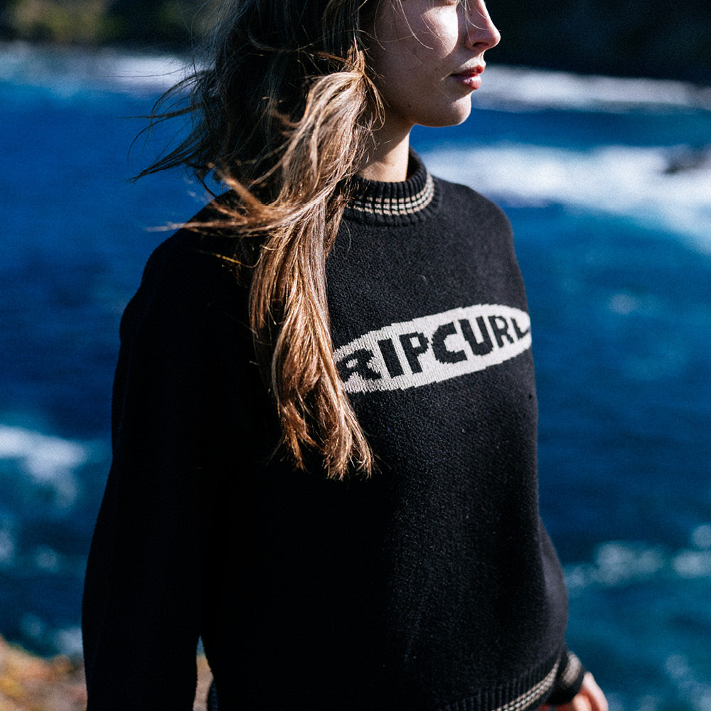Person wearing a black Rip Curl sweater with a blue water background