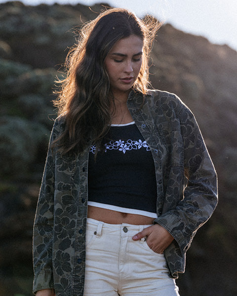 Woman wearing a black crop top with floral design and patterned jacket outdoors.