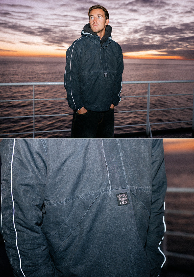 Man wearing a dark jacket with a logo against a sunset over water backdrop