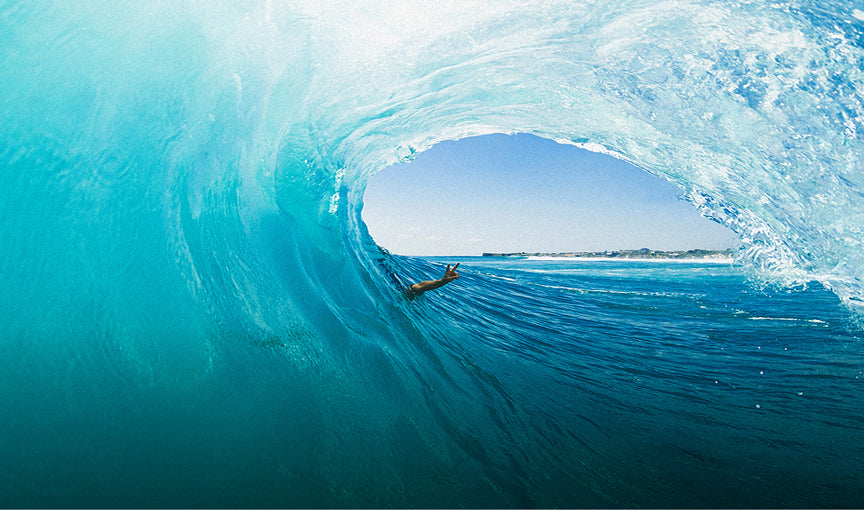 Person surfing inside a large wave with clear blue sky